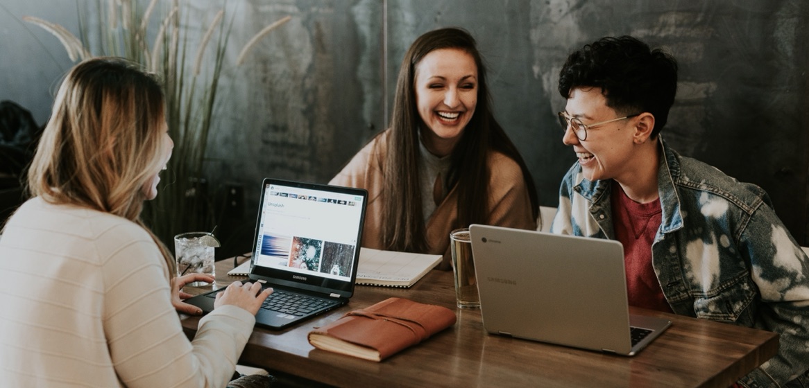 Three people laughing together at a table with laptops