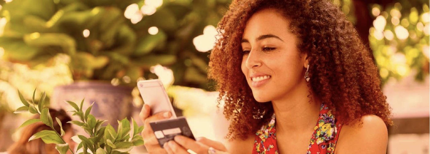 A woman smiling at her phone while holding a payment card
