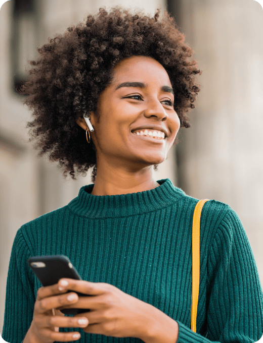A woman outdoors smiling with her phone