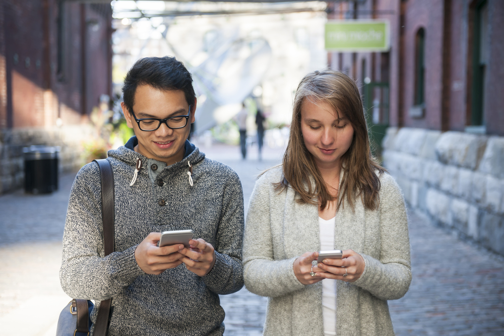 Two people looking at their phones on a city street